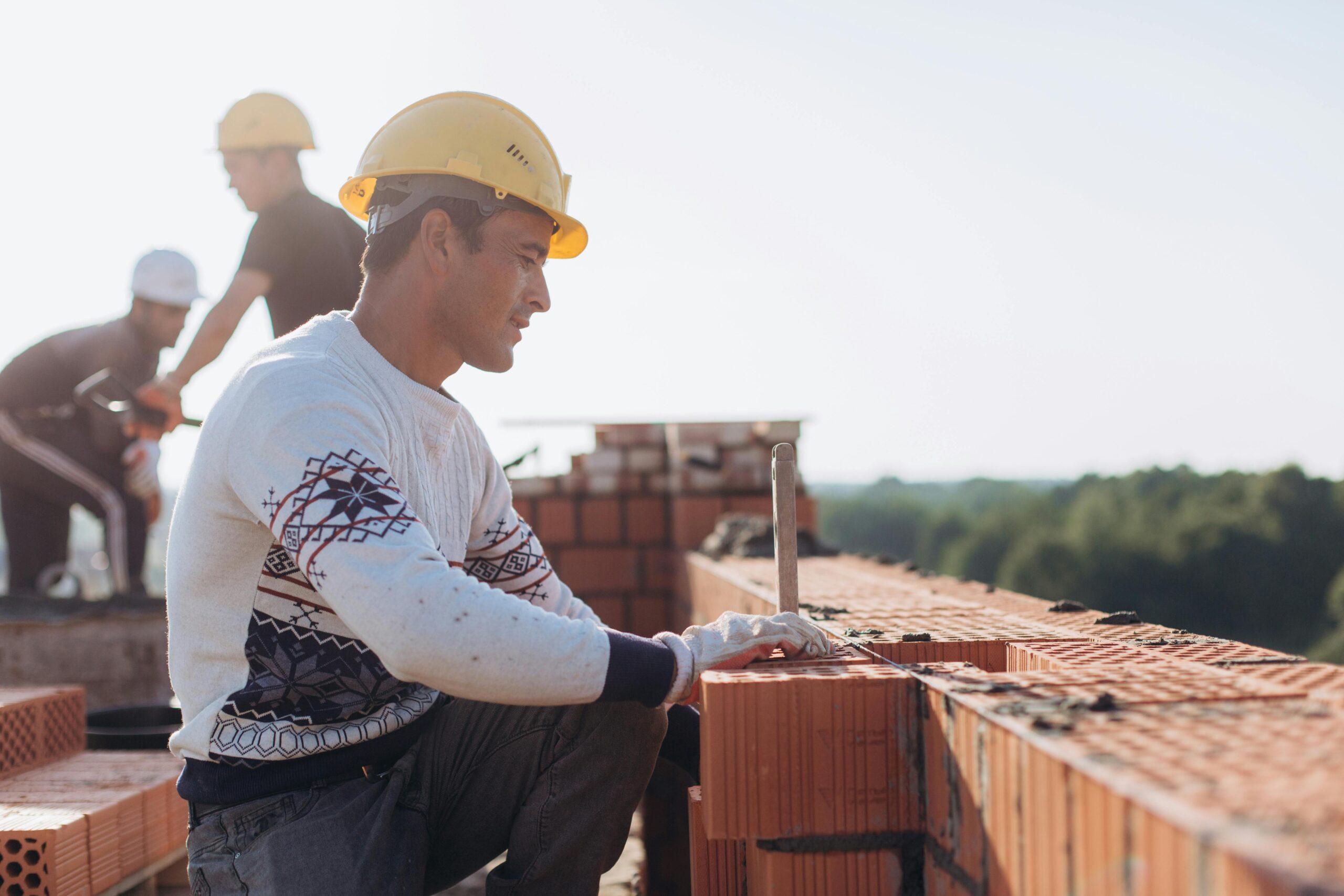 Services Construction worker laying bricks outdoors in sunny weather with lush greenery in background.
